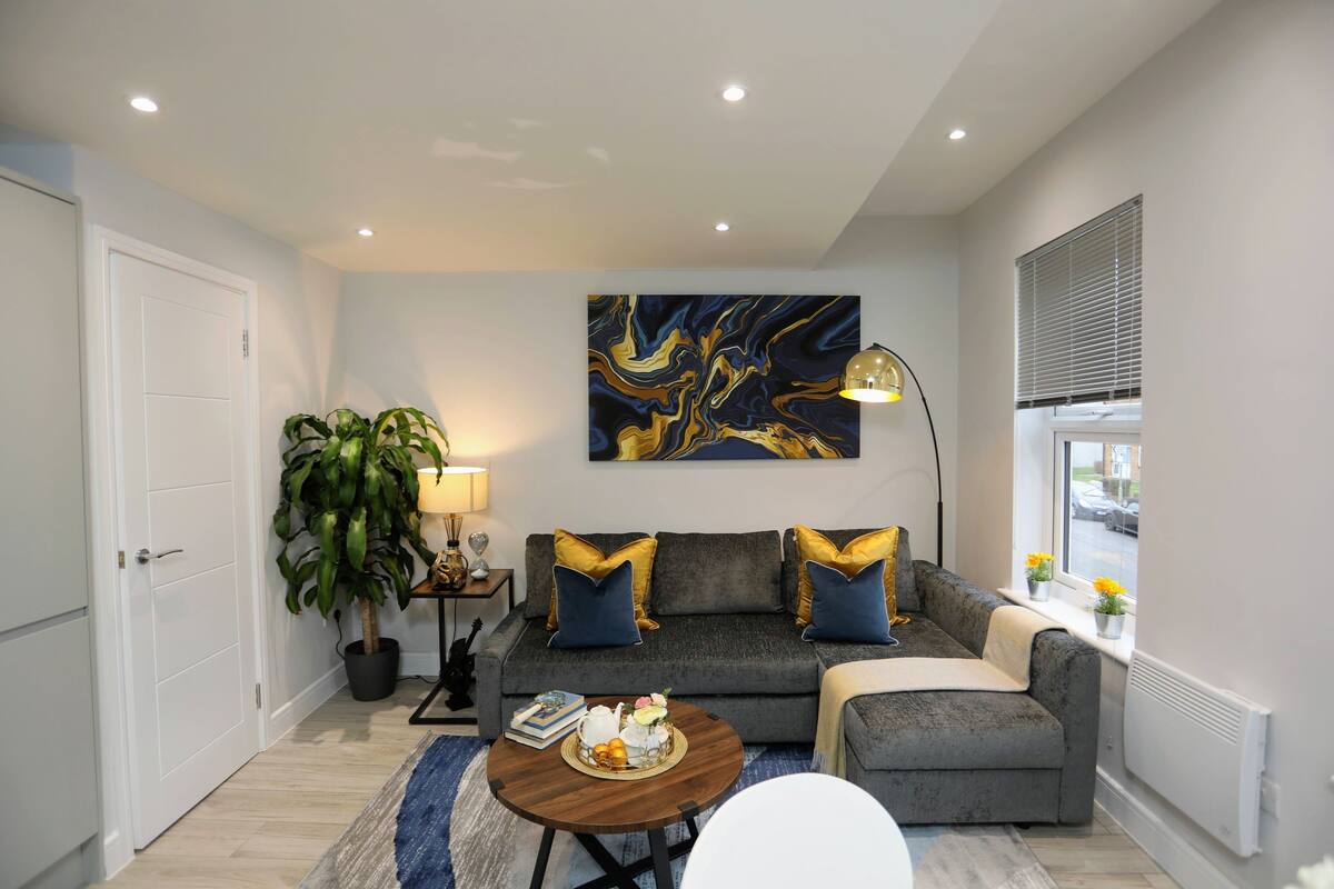 A modern living room with a grey sofa, blue cushions, a round coffee table, and a large abstract painting on the wall.