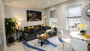 A modern living room with a grey sofa, a coffee table, a potted plant, and a painting on the wall. - Stanhope Road Apartments (London)