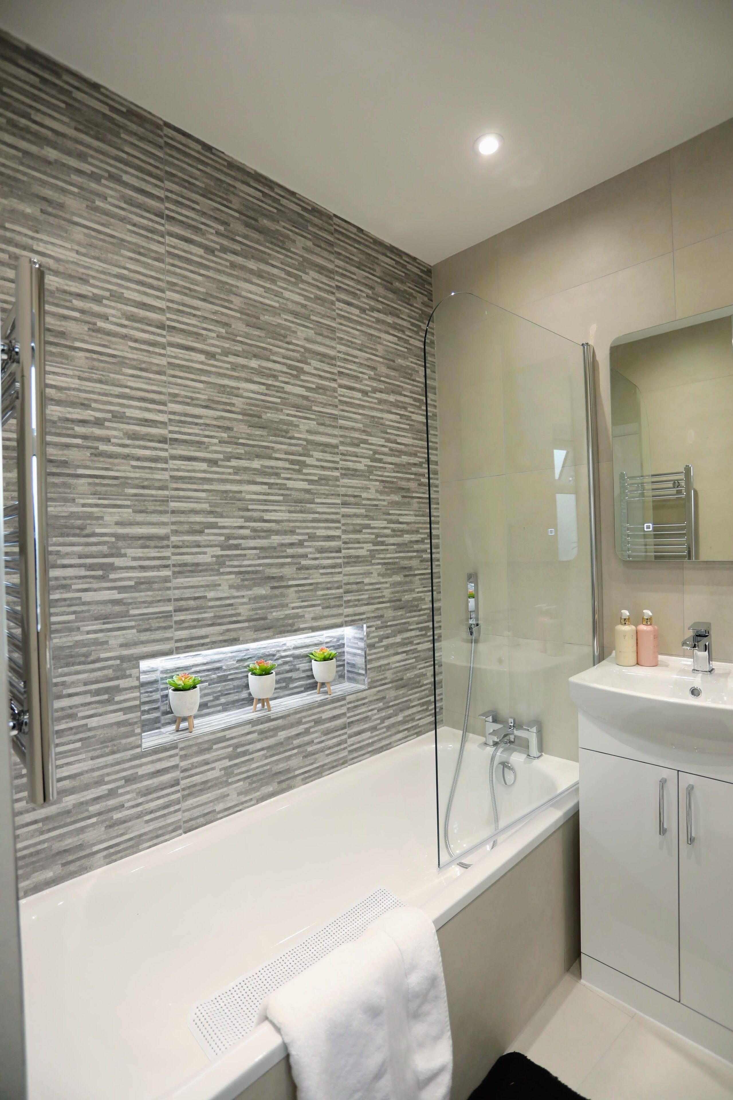 Un baño moderno con ducha envuelta en vidrio, una bañera blanca y un tocador con espejo.