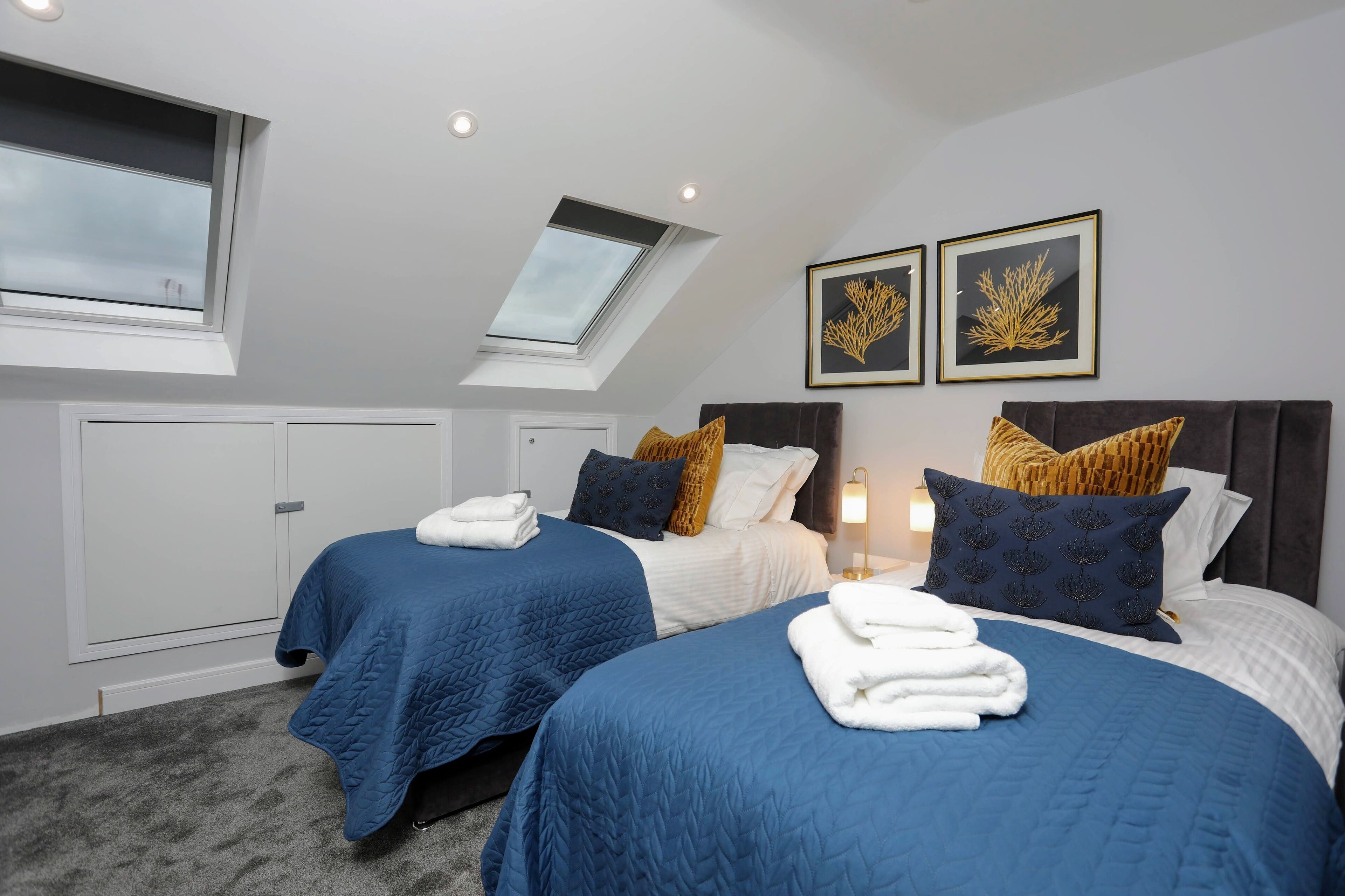 A hotel room with two beds, a skylight, and framed artwork on the wall.