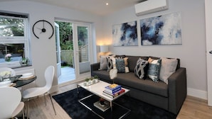 A modern living room with a grey sofa, a coffee table with books, a white chair, and abstract art on the wall. - Stanhope Road Apartments (London)