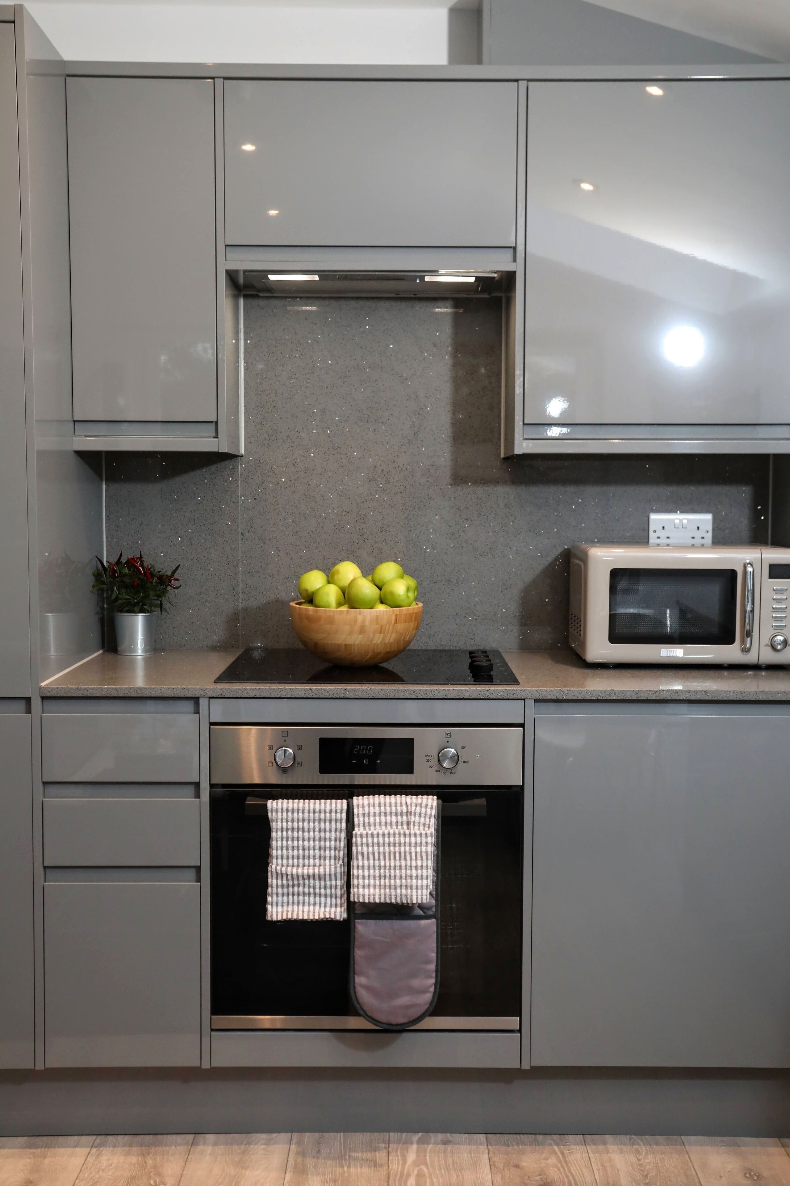 A kitchen with grey cabinets, a microwave, a stove, and a bowl of apples.