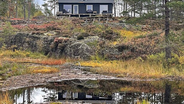 A cabin with a deck, surrounded by a natural landscape with a pond in the foreground. - 6 Person Holiday Home in Halden-by Traum (Halden)