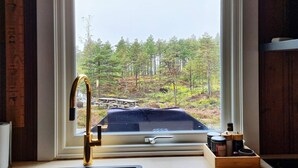 A kitchen with a window view of a forested area, a gold faucet, and a wooden spice rack. - 6 Person Holiday Home in Halden-by Traum (Halden)
