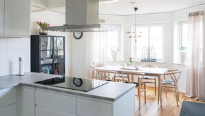 Une cuisine moderne dotée d’un îlot central, d’un coin repas avec une table et des chaises en bois, et d’une grande fenêtre agrémentée de rideaux.