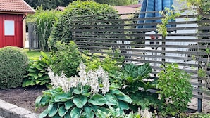 Un jardin avec une clôture en bois, diverses plantes et un bâtiment rouge.