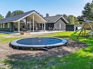 A residential backyard with a swimming pool, a covered patio, and a wooden play structure. - 5 Star Holiday Home in Blavand (Blavand)
