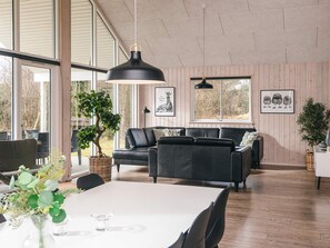 Un vaste espace de vie doté d’une grande fenêtre, d’un canapé en cuir noir, d’une table à manger et d’un luminaire suspendu.