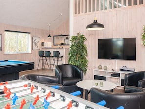 A room with a pool table, foosball table, bar area, seating, and a TV.