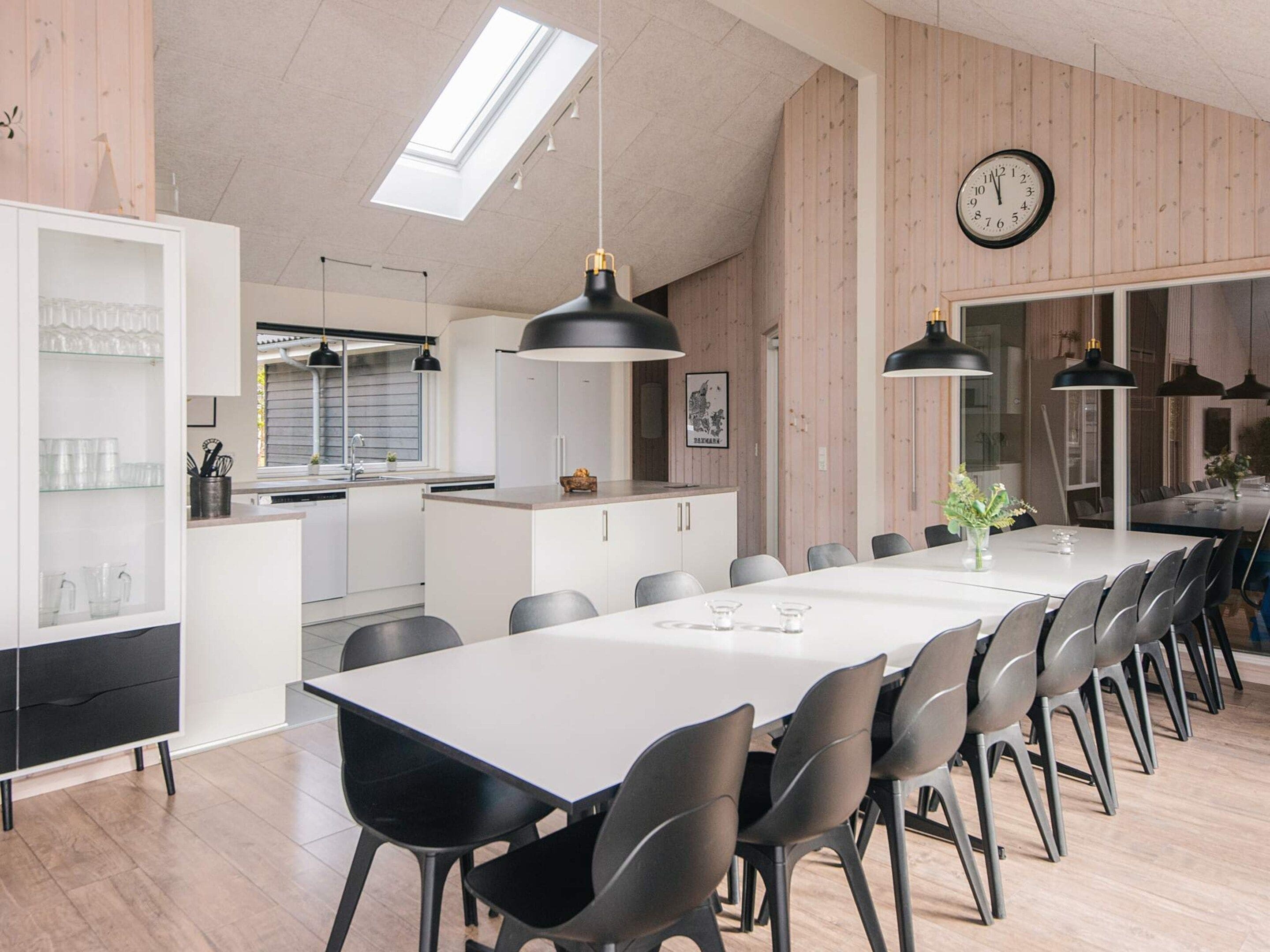Una cocina moderna con una isla central, iluminación colgante y un comedor con una mesa larga y sillas.
