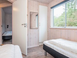 A bedroom with two beds, a wooden wall, a window, and a door leading to another room.