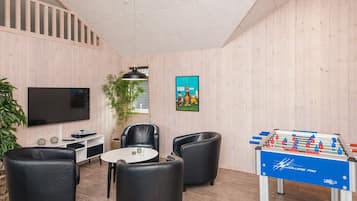 Una habitación con televisión de pantalla plana, sillones de cuero, mesa de fútbol y una planta en maceta.