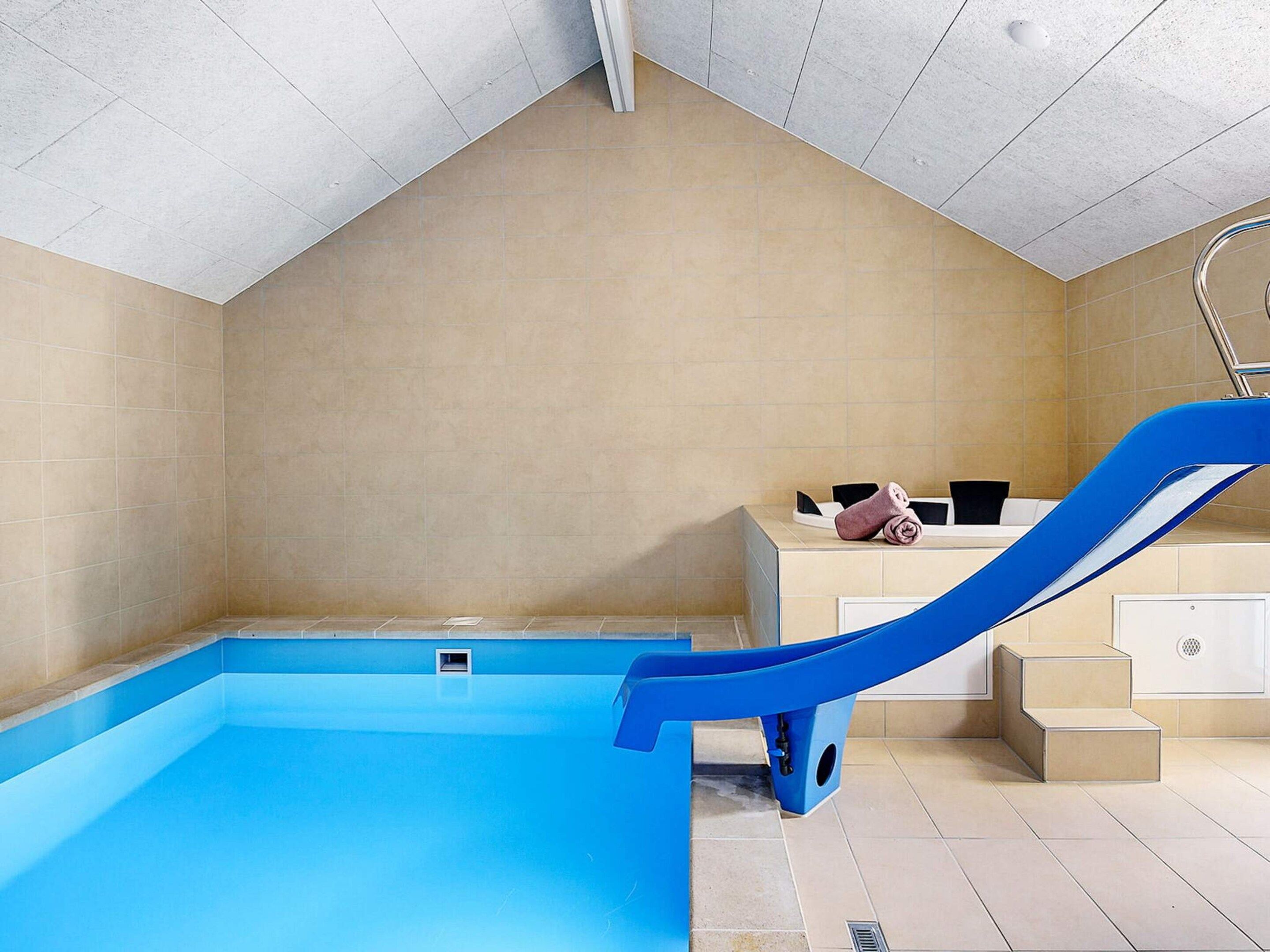 Una piscina con un tobogán azul, un ventanal pequeño y una bañera con una toalla.