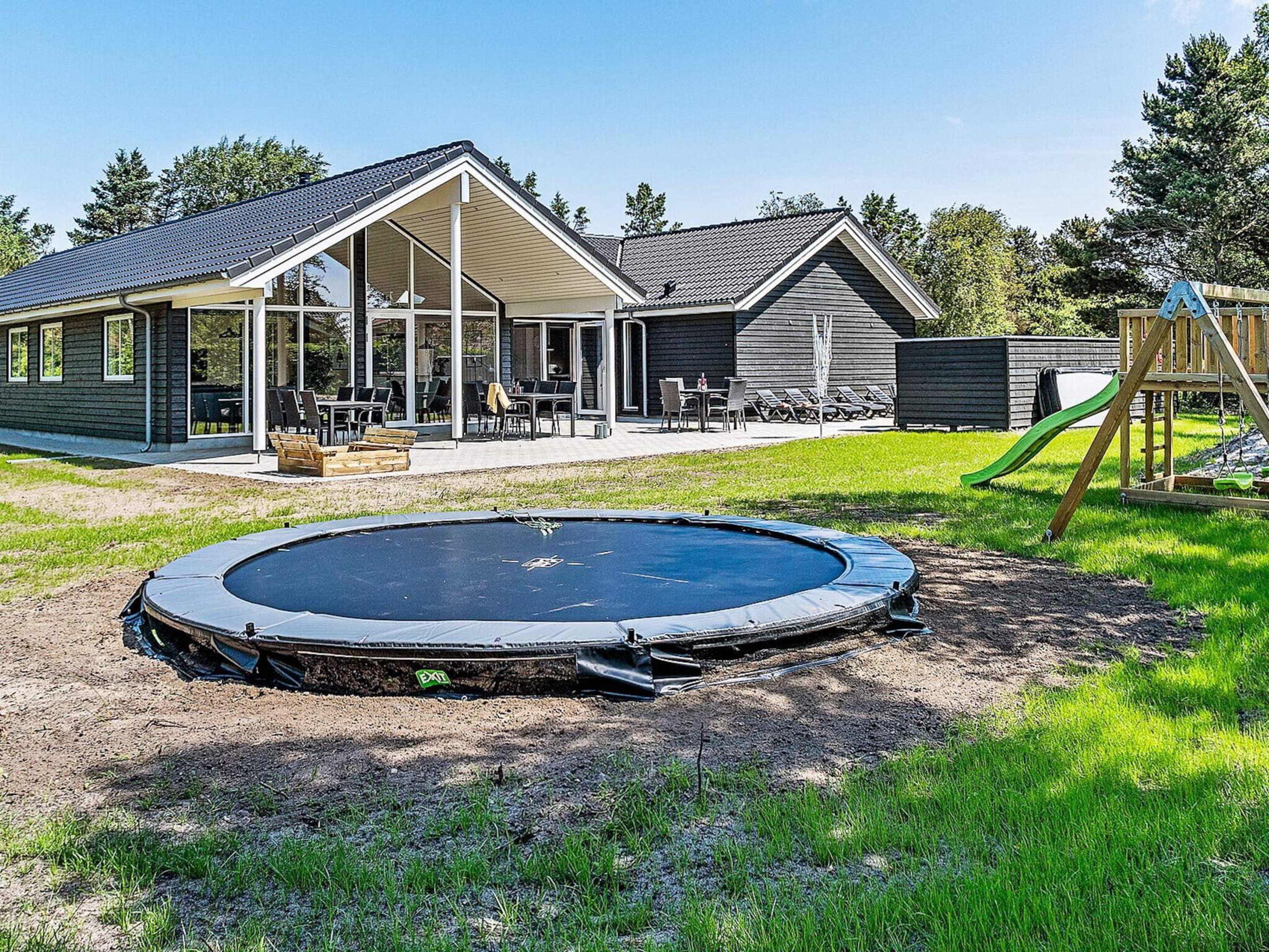 Ein Haus mit überdachter Terrasse, Trampolin und Spielgerüst.
