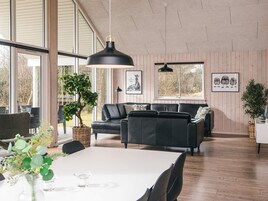 A spacious living area with a large window, a black leather sofa, a dining table, and a hanging pendant light.