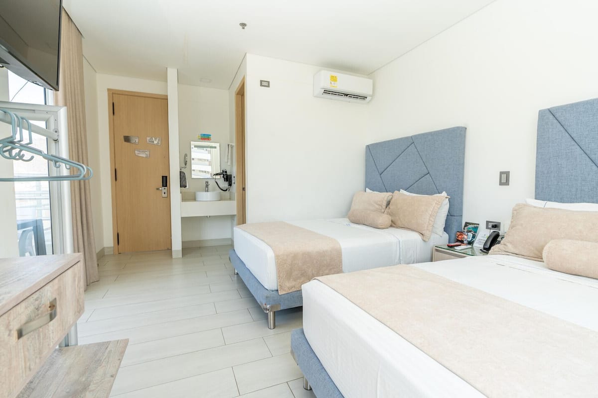 A hotel room with two beds, a bathroom, and a view of the outside.
