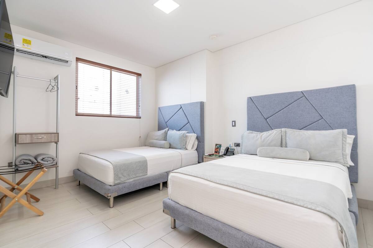 A hotel room with two beds, a TV, a desk, and a window with blinds.