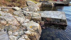 Une jetée en pierre qui s’avance dans une étendue d’eau, entourée de rochers et de végétation.
