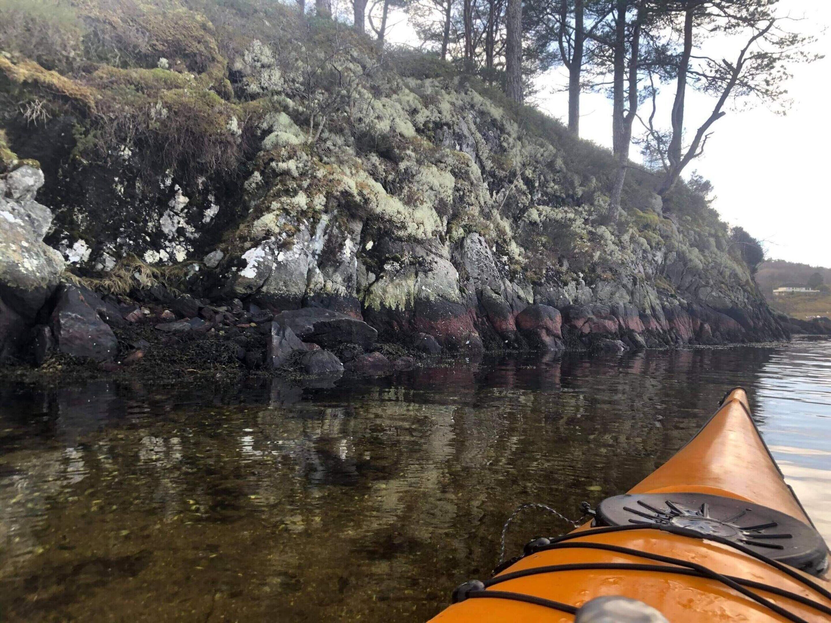 Un kayak sur une rivière paisible, avec des berges rocheuses et des arbres en arrière-plan.