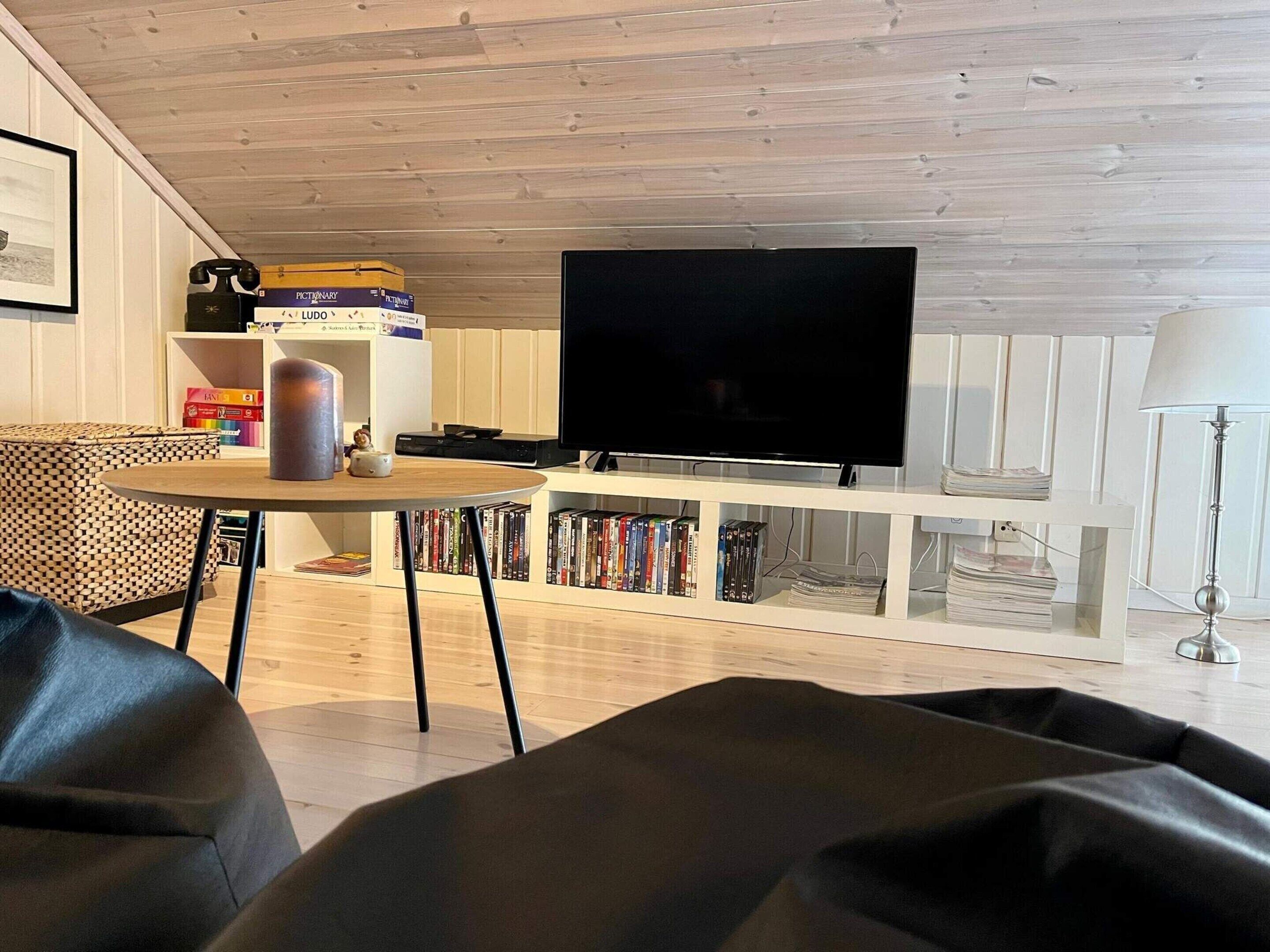 Una sala de estar con un televisor de pantalla plana, una mesa redonda de madera, una estantería y un sofá estampado.