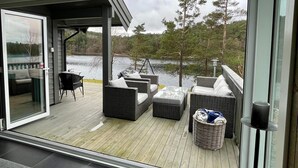 Une terrasse dotée de meubles en osier, d’une porte vitrée et offrant une vue sur un lac.