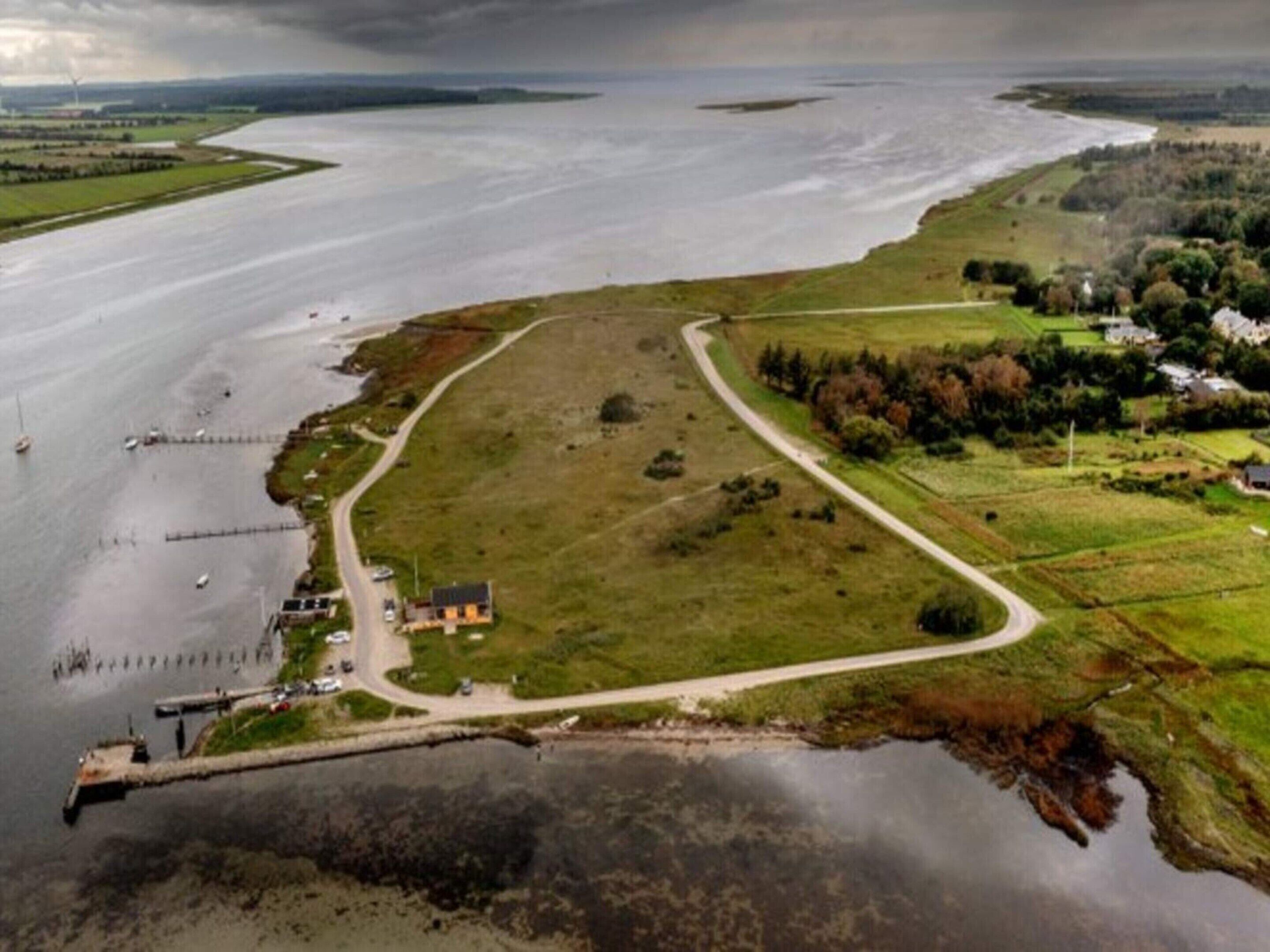 An aerial view of a coastal area with a small building, a road, and a body of water.
