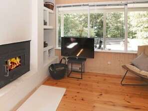 A living room with a fireplace, a television, wooden flooring, and a window with a view of trees.