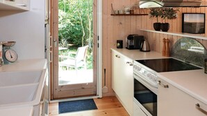 Een kleine keuken met een spoelbak, kookplaat en aanrecht, houten vloeren en een deur naar een buitenruimte.