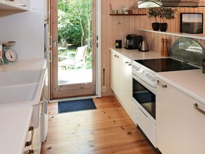 A compact kitchen with a sink, stove, and countertop, wooden flooring, and a door leading to an outdoor area.