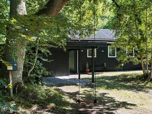 A rustic cabin with a swing set, surrounded by dense foliage.