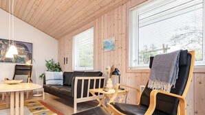 A cozy cabin interior with a wooden ceiling, a sofa, a dining table, and a chair with a blanket. - 8 Person Holiday Home in Blokhus (Blokhus)