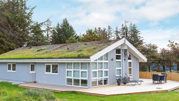 A modern house with a sloped roof, large windows, and a deck with outdoor furniture. - 8 Person Holiday Home in Blokhus (Blokhus)