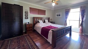 A bedroom with a wooden bed, a ceiling fan, a nightstand, a wardrobe, a window with blinds, and a patterned rug. - Scenic View Esk Escape (Esk)
