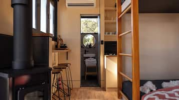 A compact, modern interior with a wood-burning stove, a kitchenette, and a cozy bed area.