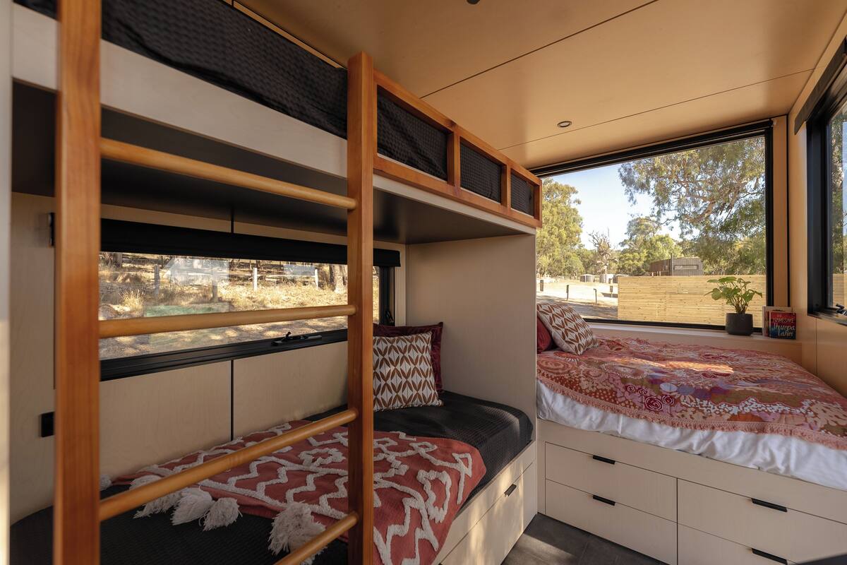 A compact, modern interior with bunk beds and a large window offering a view of the outdoors.
