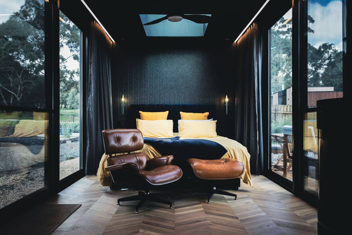 A modern bedroom with a large bed, leather chairs, and a view of the outdoors.