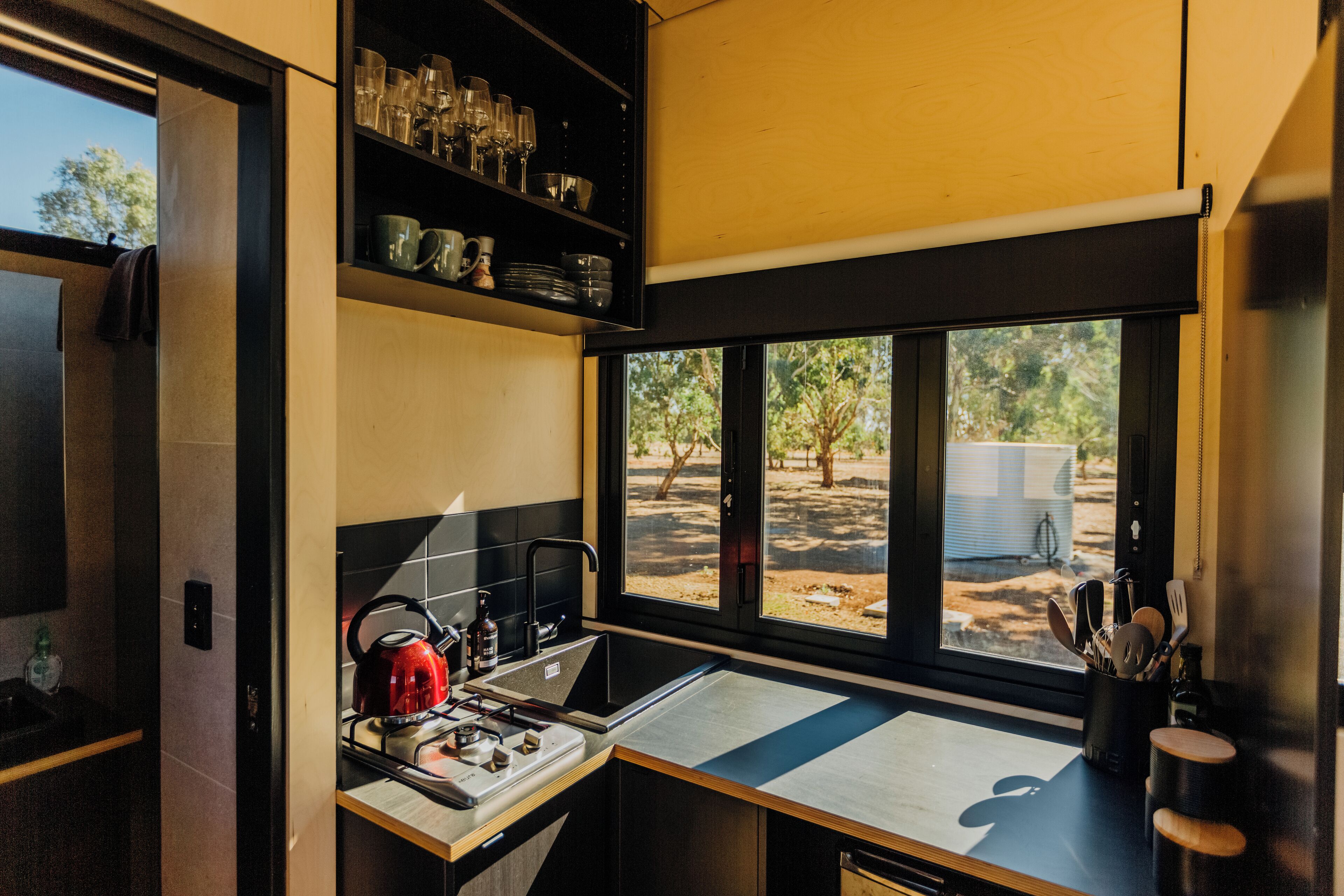 Cocina compacta con estufa, lavamanos y ventana con vista a un patio.