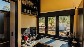 Cocina compacta con estufa, lavamanos y ventana con vista a un patio.
