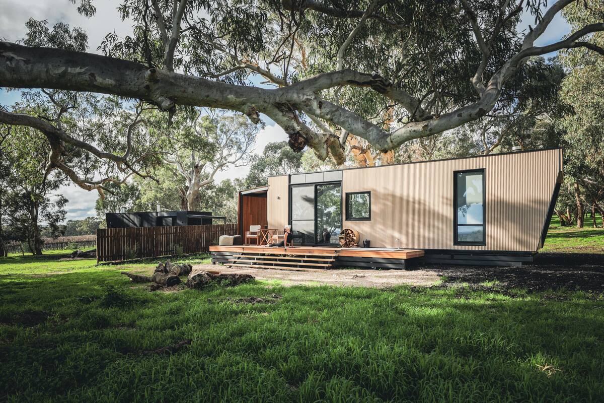 A modern, single-story cabin with a deck, large windows, and a view of the surrounding trees.