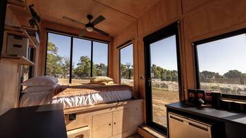 Un interior de madera acogedor con una cama, un escritorio y ventanas amplias con vistas al exterior.