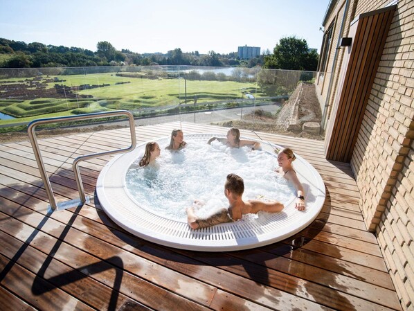 A hot tub on a wooden deck with a view of a golf course and buildings in the distance. - 5 Star Holiday Home in Borkop (Borkop)