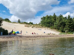 Une plage avec des tentes et des gens, une rivière et des arbres.