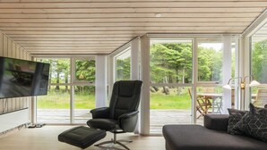 A modern living room with a large TV, comfortable seating, and a view of a deck and greenery. - 8 Person Holiday Home in Albaek (Aalbaek)