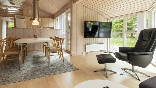 A modern interior with a wooden ceiling, a dining area with a round table and chairs, a black leather sofa, and a TV mounted on the wall. - 8 Person Holiday Home in Albaek (Aalbaek)