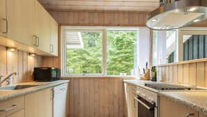 A compact kitchen with wooden cabinets, a microwave, a sink, and an oven. - 8 Person Holiday Home in Albaek (Aalbaek)