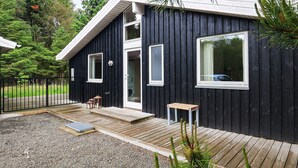 A black wooden cabin with a deck, a small table, and a bench. - 8 Person Holiday Home in Albaek (Aalbaek)