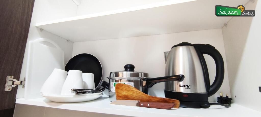 A kitchen area with a coffee maker, a pot, a knife, and white cups on a shelf.