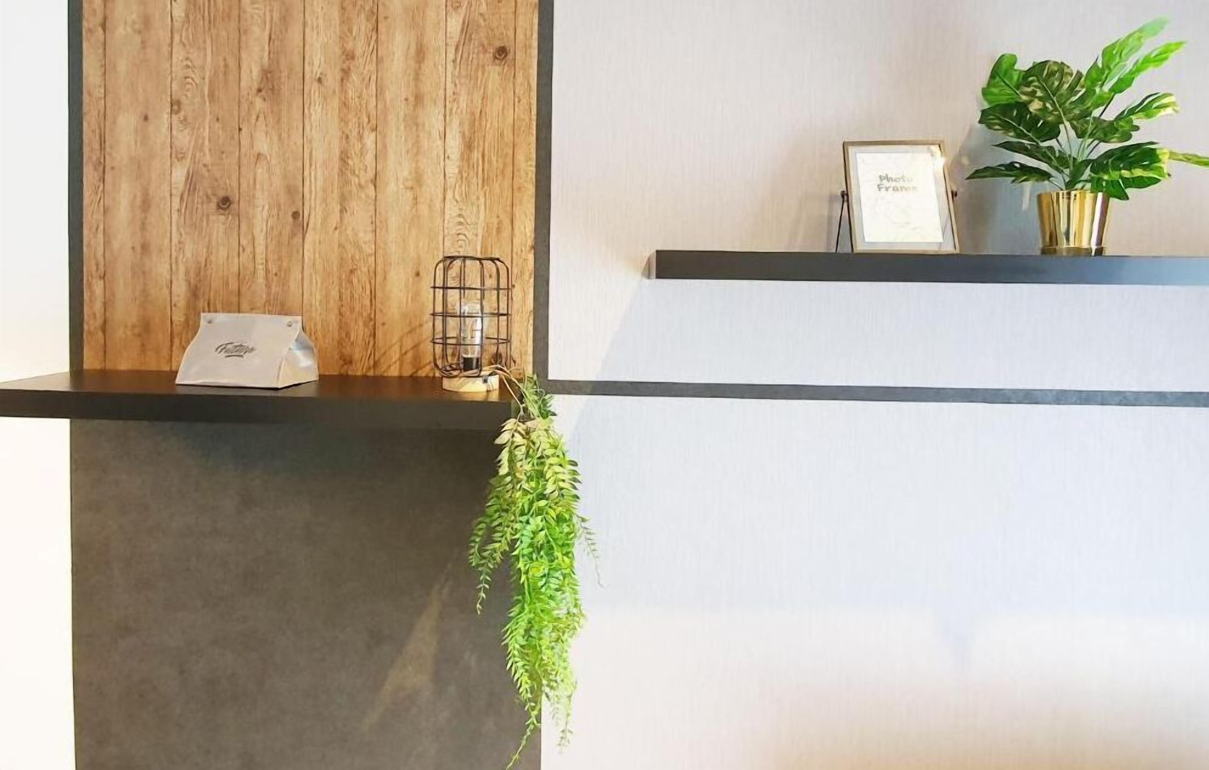 A reception desk with a wooden panel, a framed certificate, a potted plant, and a hanging plant.