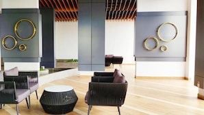 Un lobby moderno con mobiliario negro y gris, una mesa redonda central y decoración en la pared.