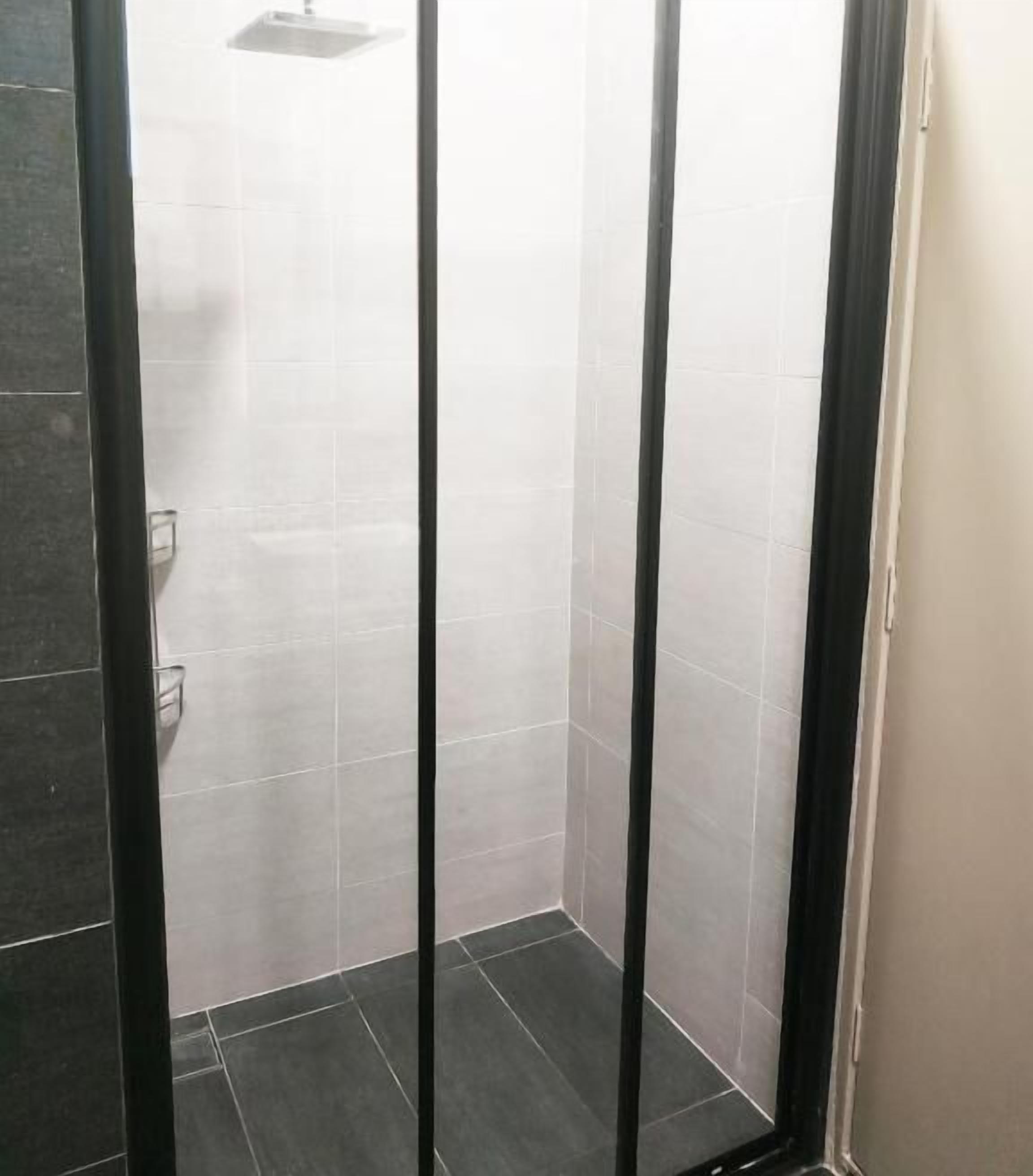 A shower area with tiled walls and floor, a black door frame, and a visible hand soap dispenser.